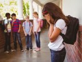 Sad schoolgirl with friends in background at school corridor