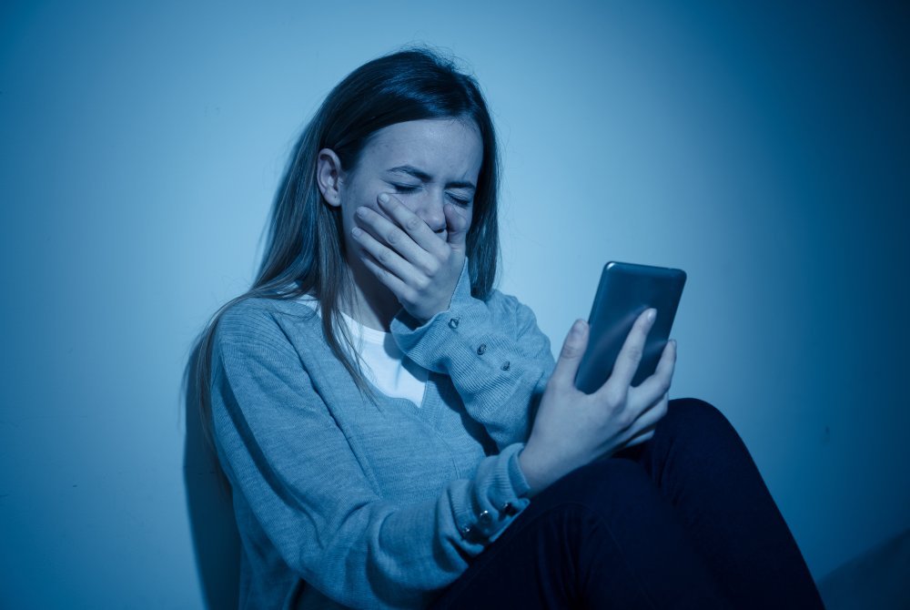 Depressed teenager girl on mobile phone victim of cyberbullying feeling sad, unhappy and lonely
