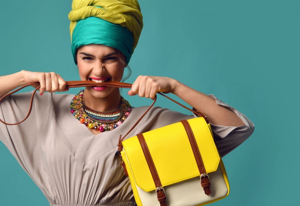 Woman yelling screaming and eating belt of hand hold stylish fashion yellow leather bag