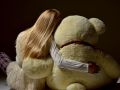 teenage girl sitting backward hugging big teddy bear back view