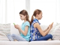 people, children, technology, friends and addiction concept - little girls with smartphones sitting