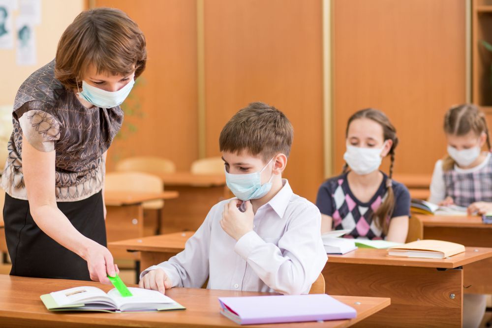 school kids and teacher with protection mask against flu virus at lesson