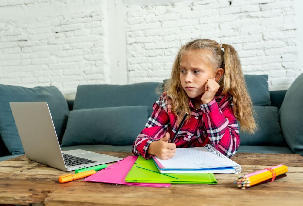 Sweet little schoolgirl having trouble with computer and homework at home