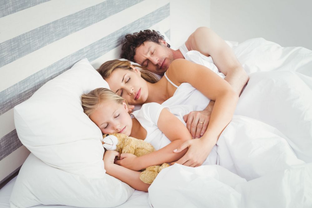 High angle view of parents sleeping with daughter on bed
