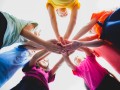 Kids putting their hands together indoors in rainbow t-shirts